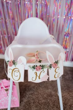 a baby crib with bunny ears and flowers on the top, next to a pink gift box