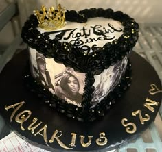 a heart shaped cake decorated with black and white frosting, gold lettering and a crown on top