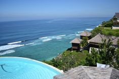 an outdoor swimming pool next to the ocean with thatched roof huts on each side