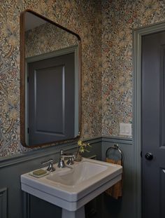 a sink and mirror in a room with floral wallpaper on the walls behind it