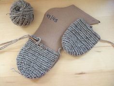 a pair of gray knitted mittens sitting on top of a wooden table next to a ball of yarn