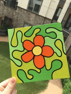 a hand holding up a piece of wood with a flower painted on it