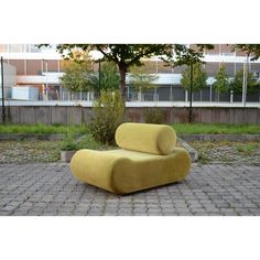 a large yellow chair sitting on top of a brick floor next to a green tree