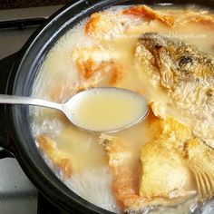 a spoon in a pot filled with soup and fish on top of the stovetop