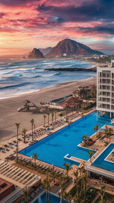 an aerial view of the beach and pool area at sunset with mountains in the background