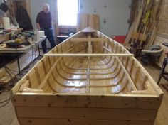 a man standing next to a wooden boat in a room filled with woodworking supplies