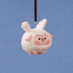 a white stuffed animal hanging from a black string on a blue background with a brown cord