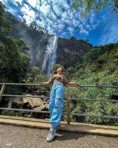 a woman standing in front of a waterfall with her arms spread out to the side