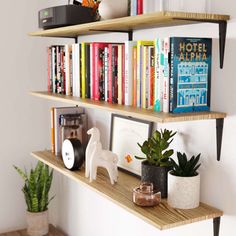 three wooden shelves with books, plants and pictures on them next to a white wall