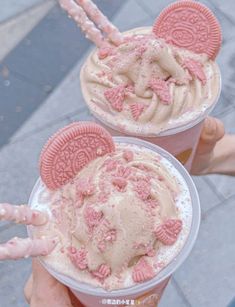 two people holding up pink and brown ice creams with oreo cookies on top