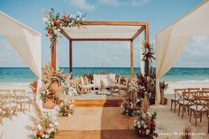 an outdoor wedding setup on the beach with white draping and floral arrangements in front of the ocean