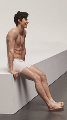 a shirtless man sitting on top of a white wall