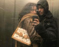 a man and woman standing in front of a mirror holding up their cell phones to take a selfie