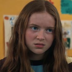 a close up of a person with long hair and blue eyes in front of a yellow wall