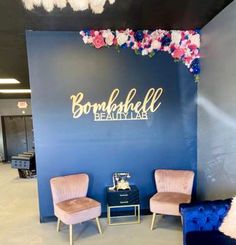 two chairs are sitting in front of a wall with flowers on it and the words, bombshell beauty lab