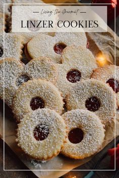 cookies with powdered sugar and jelly are on a wooden cutting board, surrounded by other pastries