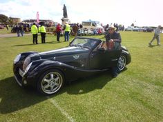 a man sitting in the driver's seat of a vintage sports car at a car show