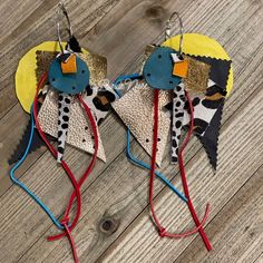 two pairs of bird shaped earrings with red, white and blue thread on them sitting on a wooden surface