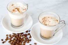 two cups filled with coffee sitting on top of white saucers next to spoons