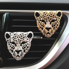 two gold and silver leopard head brooches sitting on the dashboard of a car