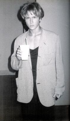 black and white photograph of a woman holding a cup in her hand while standing next to a wall