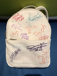 a white purse with writing on it sitting on top of a blue table next to a green wall