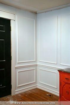 an empty room with white walls and wood floors, black door and red cabinet in the corner