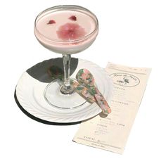 a drink in a wine glass on a plate with a menu and utensils