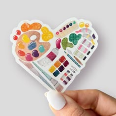 a hand holding up a heart shaped sticker with lots of different colors on it