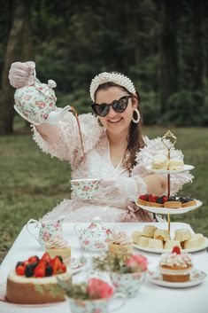 a woman sitting at a table with tea cups and cakes on it, wearing sunglasses