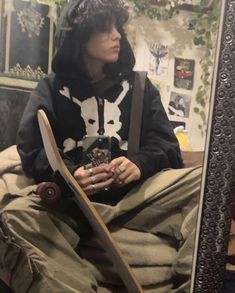 a person sitting in front of a mirror with a skateboard on their lap and wearing a hoodie