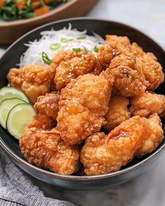 a bowl filled with fried chicken next to rice and cucumber