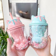 two people holding up cups with pink and blue frosting on them, one has a cat shaped lid