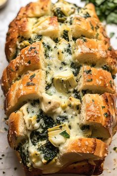 bread with cheese and spinach on it is sitting on a white surface next to some herbs