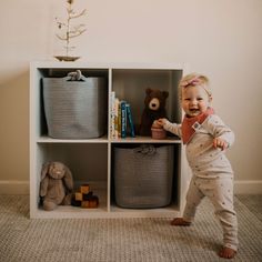 a toddler standing in front of a shelf with baskets and stuffed animals