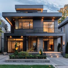 a large modern house with lots of windows and lights on the front porch, along with steps leading up to the second floor