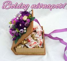 a box filled with chocolates and flowers on top of a white table covered in purple ribbon