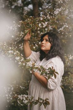 a woman standing in front of a tree with white flowers