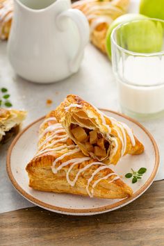 two pastries on a plate next to a glass of milk and some apples in the background