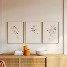 three paintings on the wall above a dresser with bowls and vases in front of it