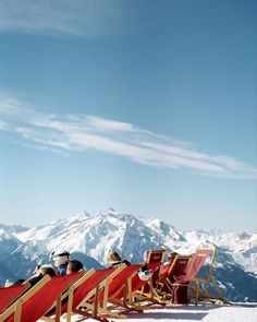 two people sitting in chairs on top of a snow covered slope with mountains in the background