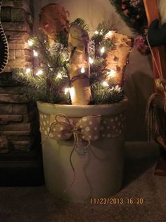 a potted plant with christmas lights in it sitting next to a fire place and fireplace