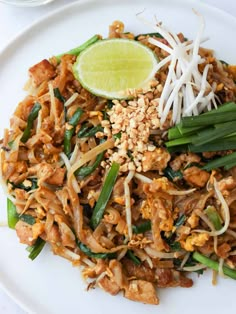 a white plate topped with pad thai noodles and meat, garnished with sliced green onions