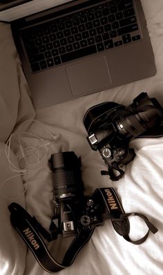 a laptop computer sitting on top of a bed next to a pair of camera's