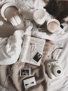 an open book, camera, headphones and other items on a bed with white sheets