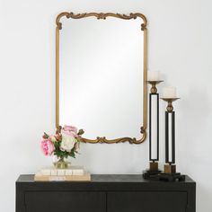 a black dresser topped with a mirror next to a vase filled with flowers and candles