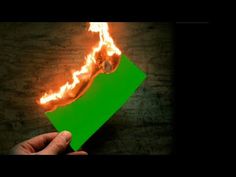 a hand holding a green piece of paper with flames coming out of it