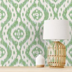 a lamp sitting on top of a wooden table next to a green and white wallpaper