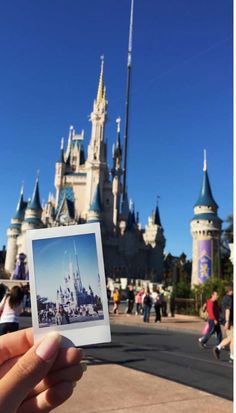 a person holding up a polaroid photo in front of the castle at disney world