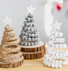 three small christmas trees made out of rope and beads on a wooden table with white stars in the background